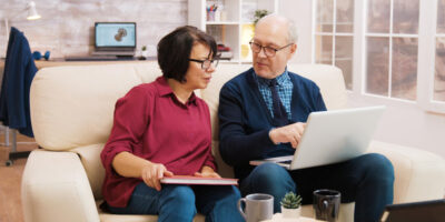 a couple using laptop and sitting on a sofa