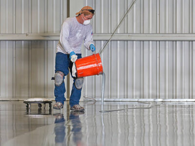 A construction worker pours paint onto a warehouse floor.