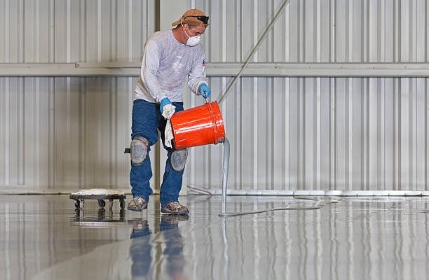 A construction worker pours paint onto a warehouse floor.