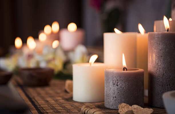 Closeup of burning candles spreading aroma on table in a spa room. Beautiful composition with grey and white candles for spa treatment. Zen and relax concept.